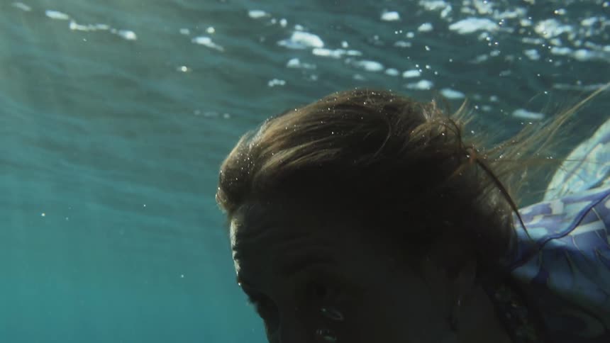 A woman holds her breath under clear deep blue water