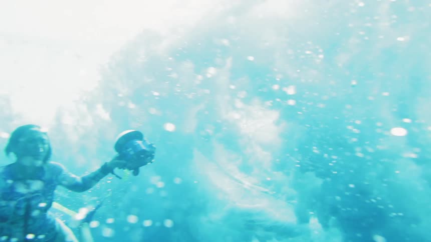 A wave rolls over a woman diving underwater