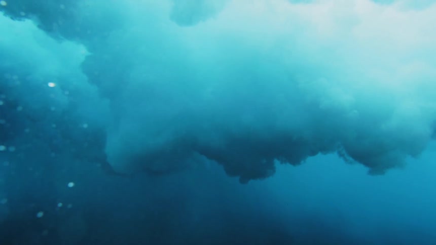 Underwater footage of a female diver swimming under a crashing wave in the blue ocean waters