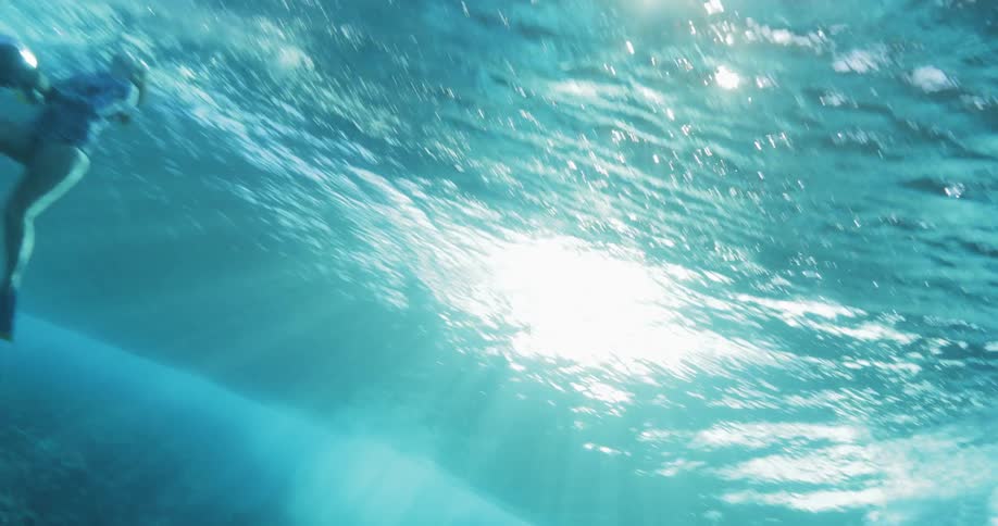 An ocean wave rolls towards a pair of underwater camera operators swimming near the surface