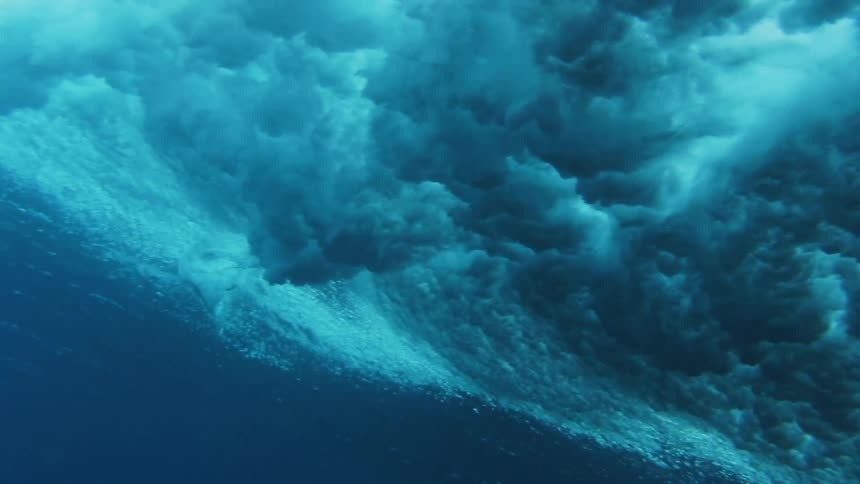 Underwater footage of a surfboard riding a wave on the blue ocean waters