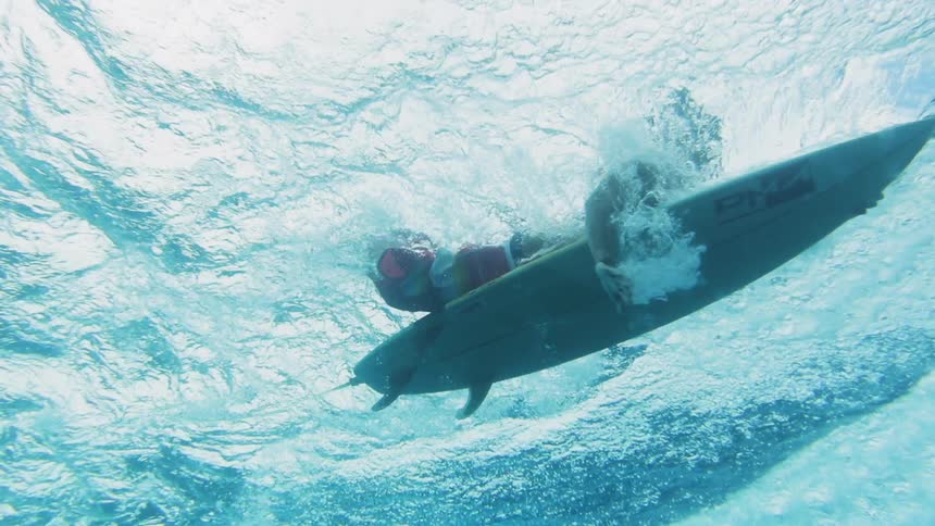Underwater footage of surfers paddling over blue ocean waves
