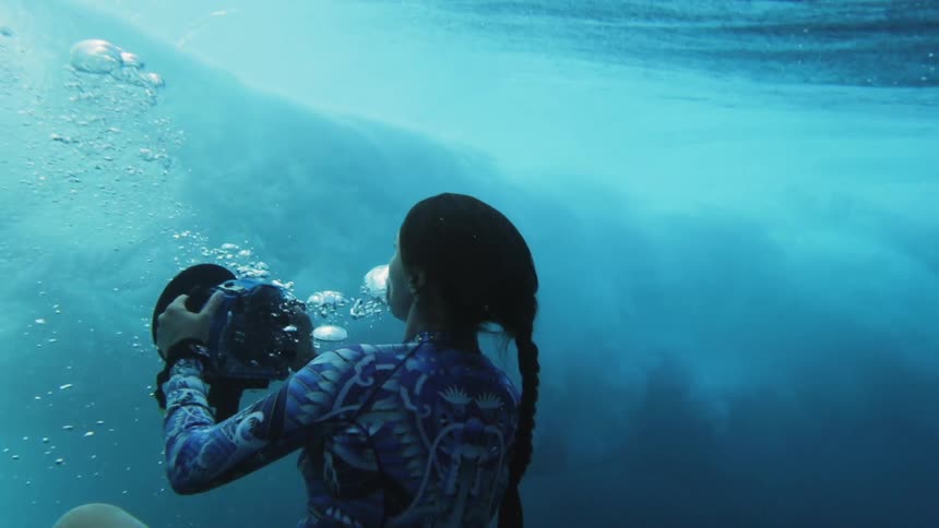 Woman takes underwater pictures of waves rolling over her while swimming in the blue ocean waters