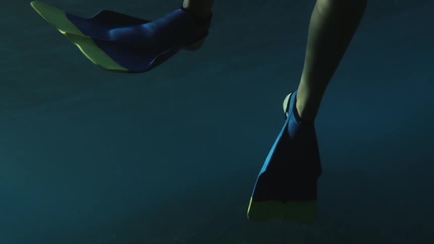 A woman wears blue swim fins while swimming underwater
