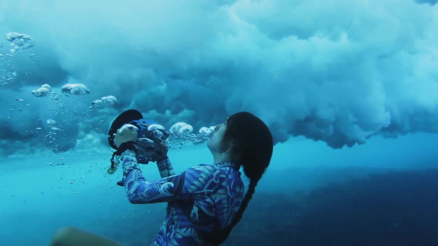 A woman swimming underwater films waves rolling over her head