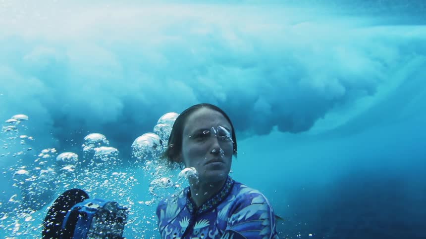 A woman swimming underwater with a camera with waves above