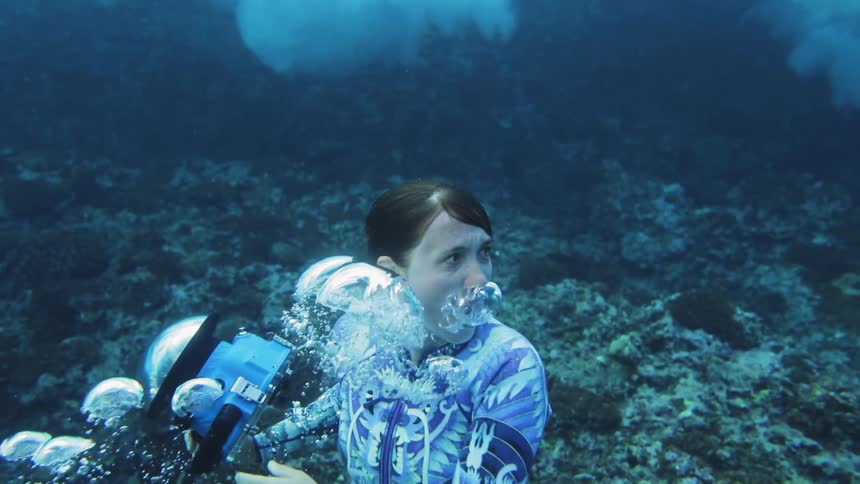 A woman swimming under water with a camera