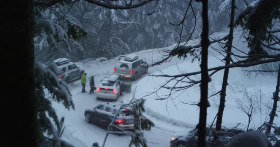 Multiple vehicles are stopped along a snow covered mountain road