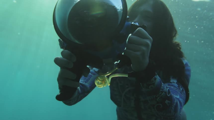 A woman swims through clear water with a camera