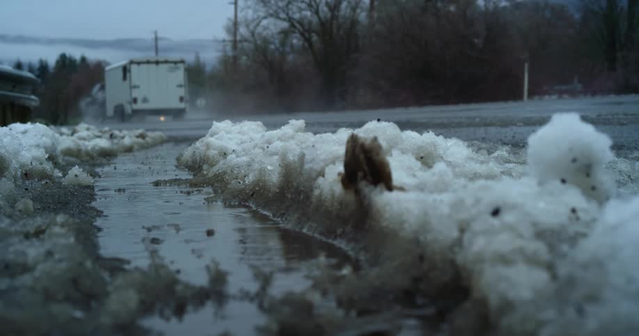 Rain falls onto muddy snow on the side of the road on a gloomy day