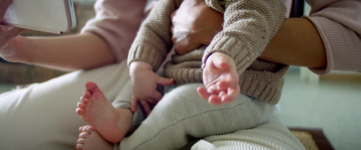 A woman holds her baby in her lap and reads on her tablet