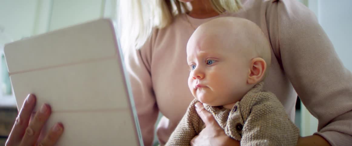 Woman holds baby as well as tablet they are both viewing