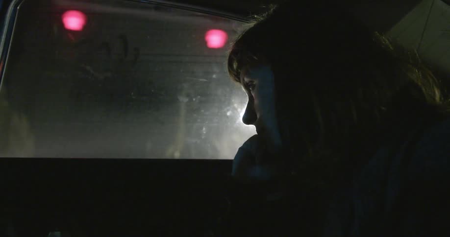A woman rides in the back of a car and bites her fingernails