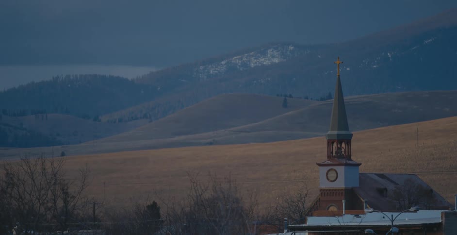 A church with a steeple sitting near plains and mountains
