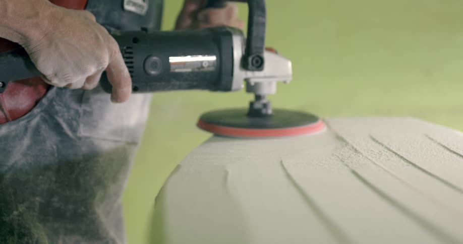 A male using a sander to sand a piece of hard material