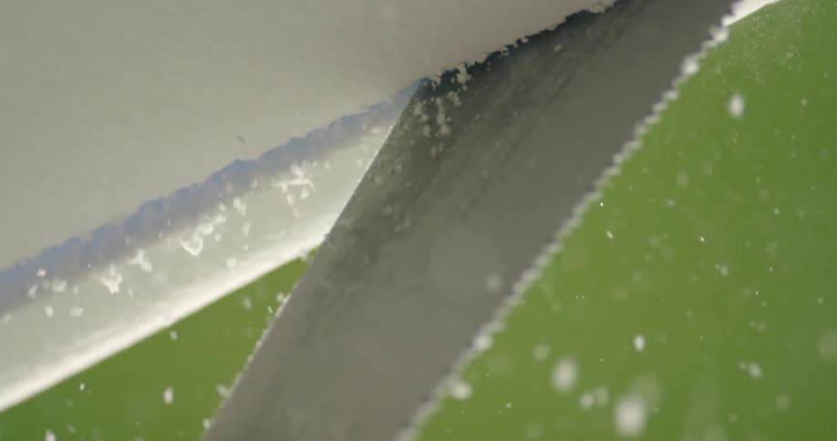 A small saw blade cuts through a piece of foam board which releases many particles