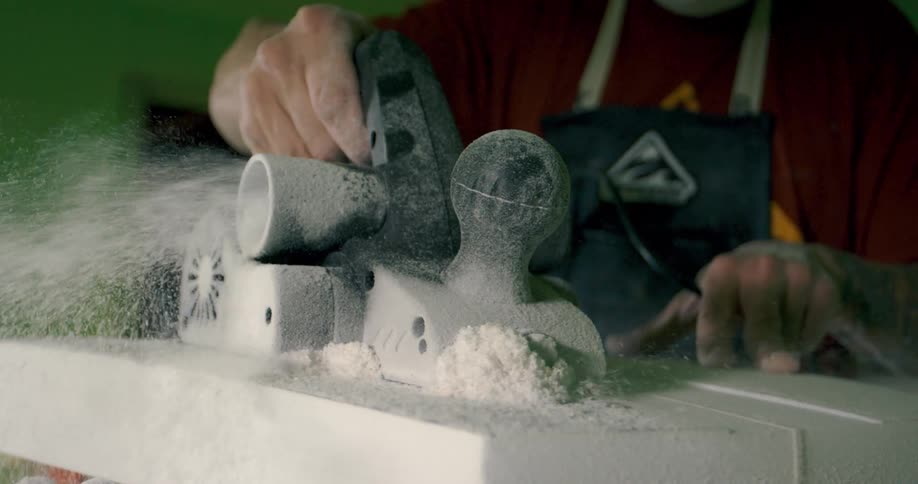 A man uses a power tool to smooth the surface of a piece of polymeric foam