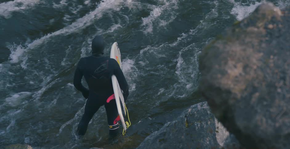 A man with a wetsuit holding a surfboard in a rocky coast with water