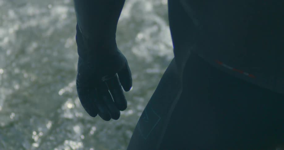 A man in a wet suit stands and looks down at a river