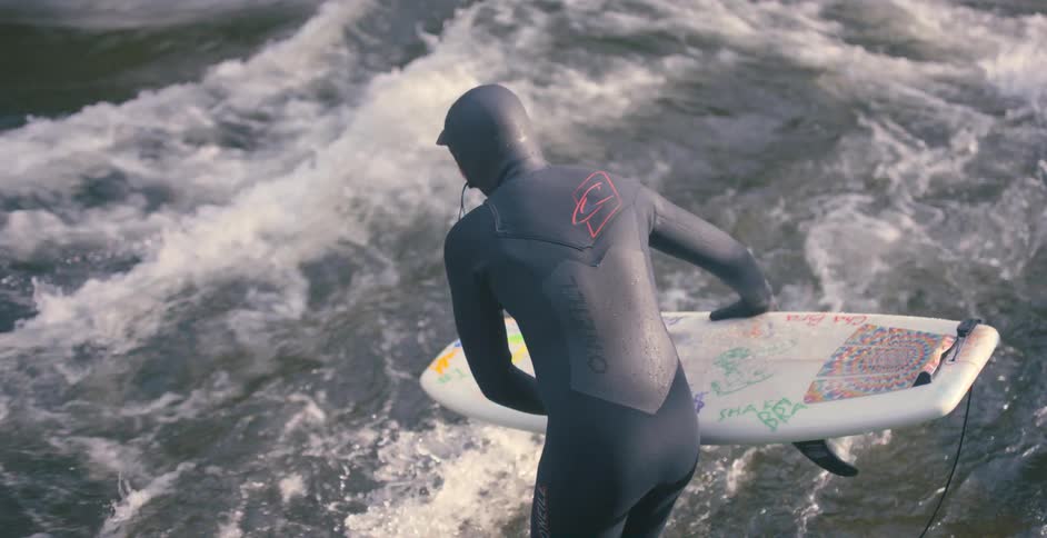 A man in a gray full body swim suit jumps on a boogie board into the ocean