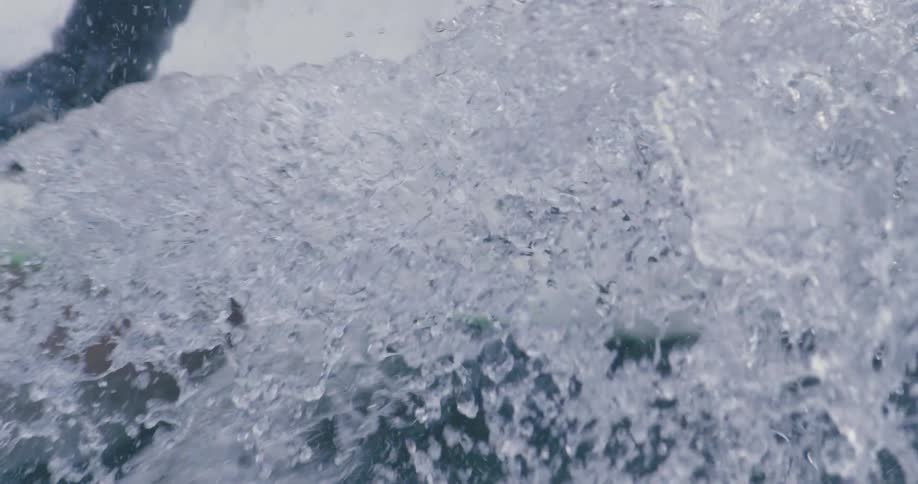 A surfer wearing a black wet suit and shoes rides a heavy wave on a striped colorful surfboard