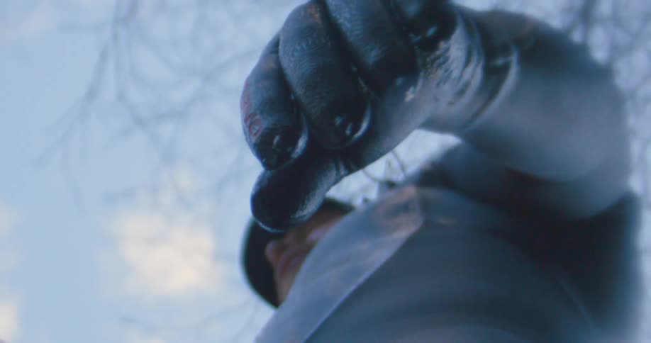 A man with a wetsuit with water dripping off his fingertips with trees the sky and clouds above