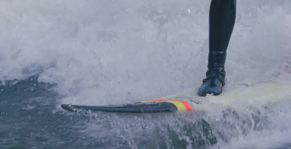 Person wearing wet suit and shoes surfs on board with bright stripe accent colors