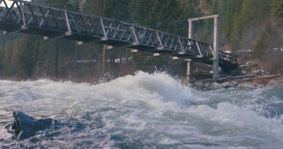 A group of surfers carry their surfboards as the walk across a bridge across a river