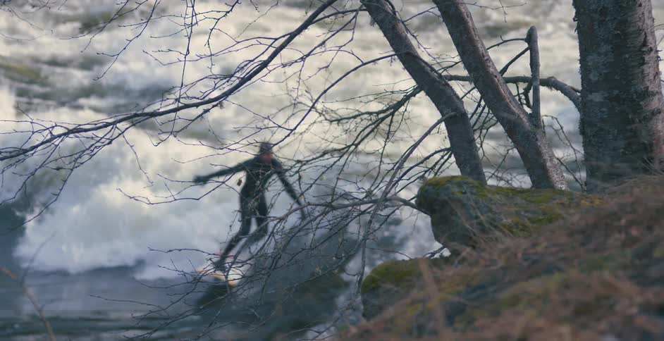 Man wearing black wetsuit surfs over the waves of a river