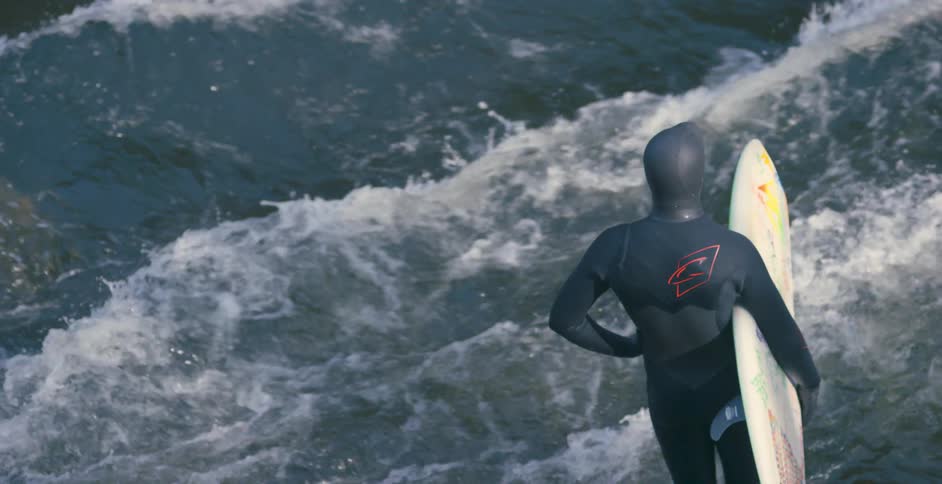A surfer in a wet suit standing next to gushing water