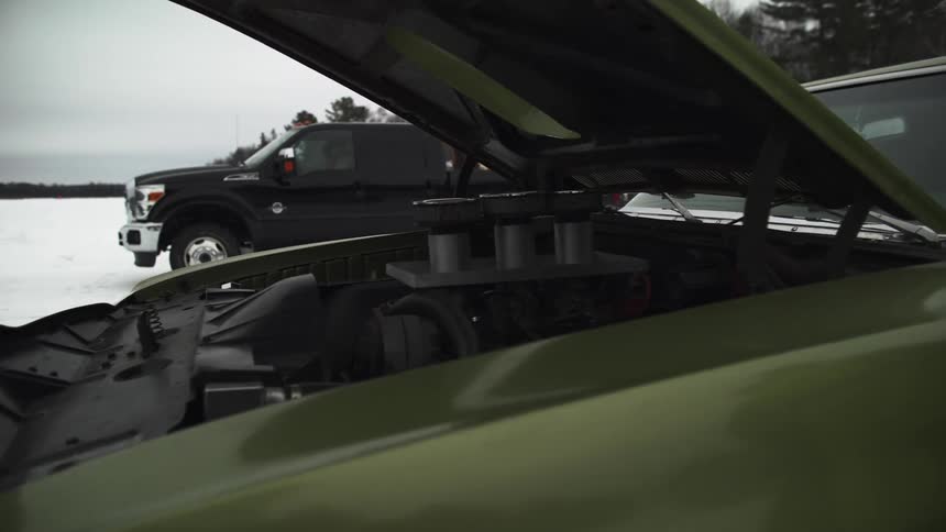 Engine of green classic car is shown off with the hood open in a snow covered lot