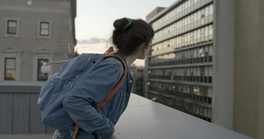 A woman with dark hair looks over the edge of a building