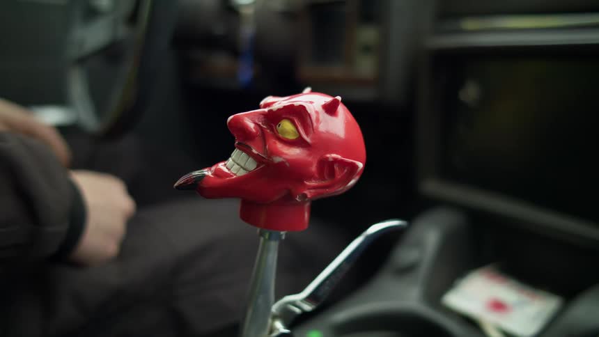 A man sitting in a vehicle with a devils head on the gear shift