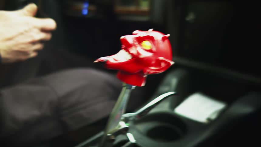 A man drives a fast car with a gear shift with a plastic devils head on top of it