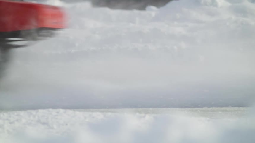 A vehicle driving on a road covered in snow with trees and the sky in the background