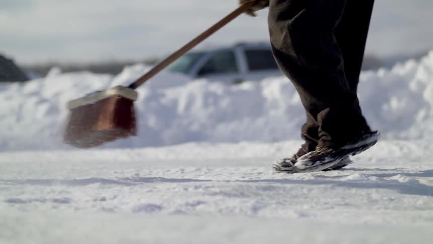 Man brushes the snow with a broom in a recently plowed road