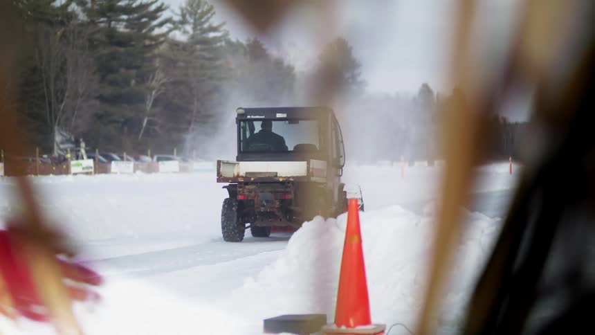 Snow plow plows the snow off the road while a pedestrian walks by