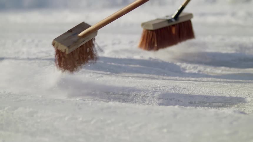 Group of men sweep the snow on a racing track with brooms