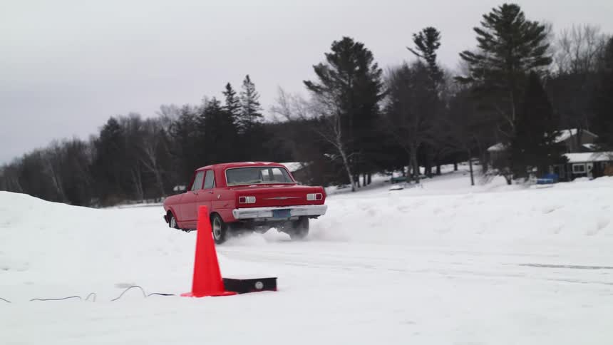 A red muscle car idles on a snow covered road before speeding off