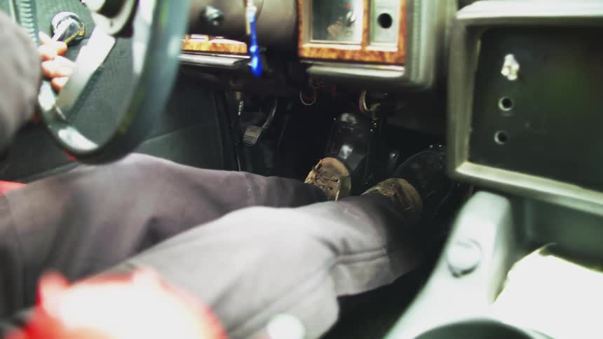A person driving turning a vehicle steering wheel with their foot on the pedals