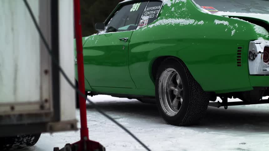 A green car is parked in the snow during midday