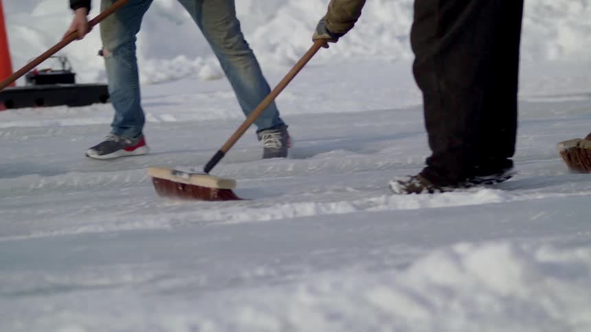 Group of men brush the snow on the surface of a race track with brooms