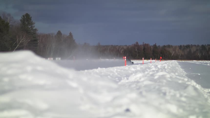 A driver rides a go kart through a snow covered field with a path plowed