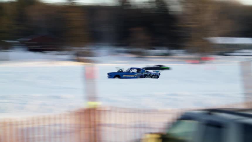 Cars drag racing in the snow with trees and the sky in the background