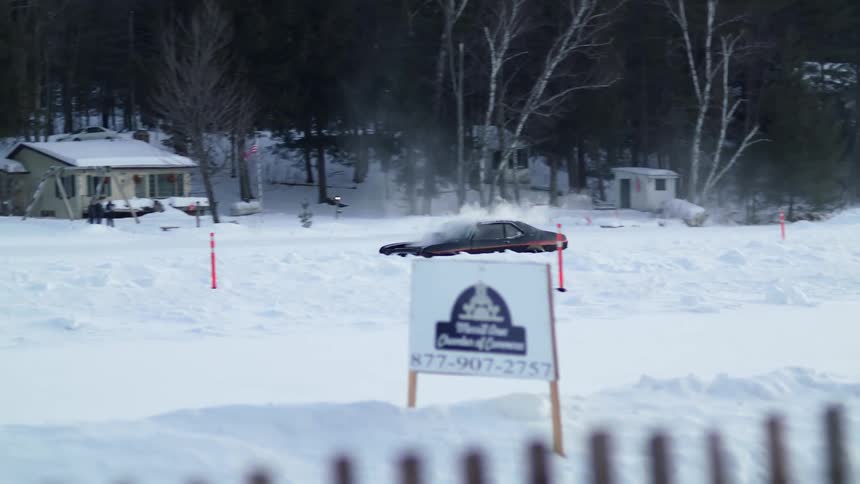 A car drives down a snow covered road near some houses