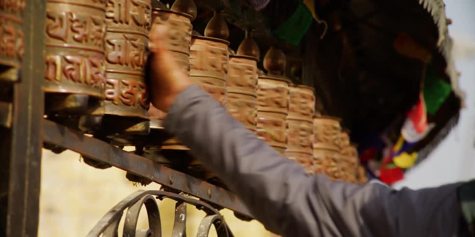 Man walking on the street spins tibetan prayer wheels near a temple