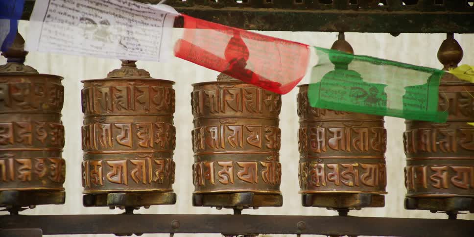 Woman pushes tibetan prayer wheels under colorful flags while walking on the street