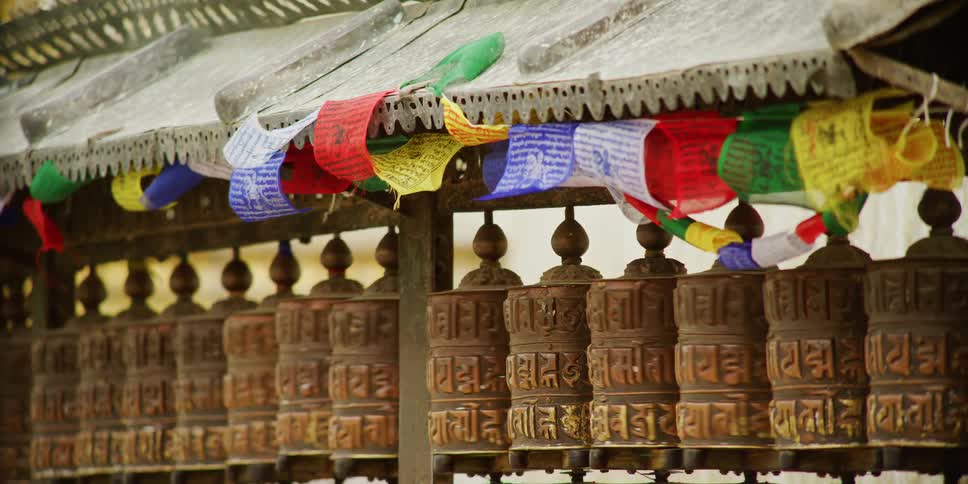 Row of prayer wheels spinning under the colorful flags on a temple in tibet