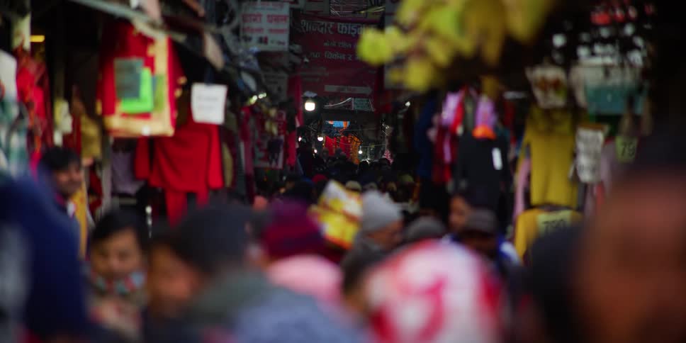 Pedestrians travel along a densely crowded street in a city during the day
