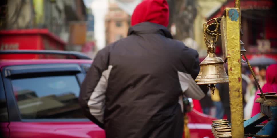 A man walks by a bell and rings it on a busy city street